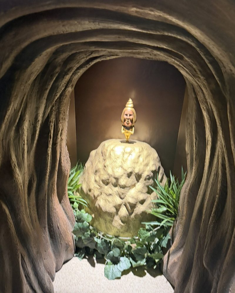 A cave-like tunnel leading to a golden Kobito figure standing on a rock