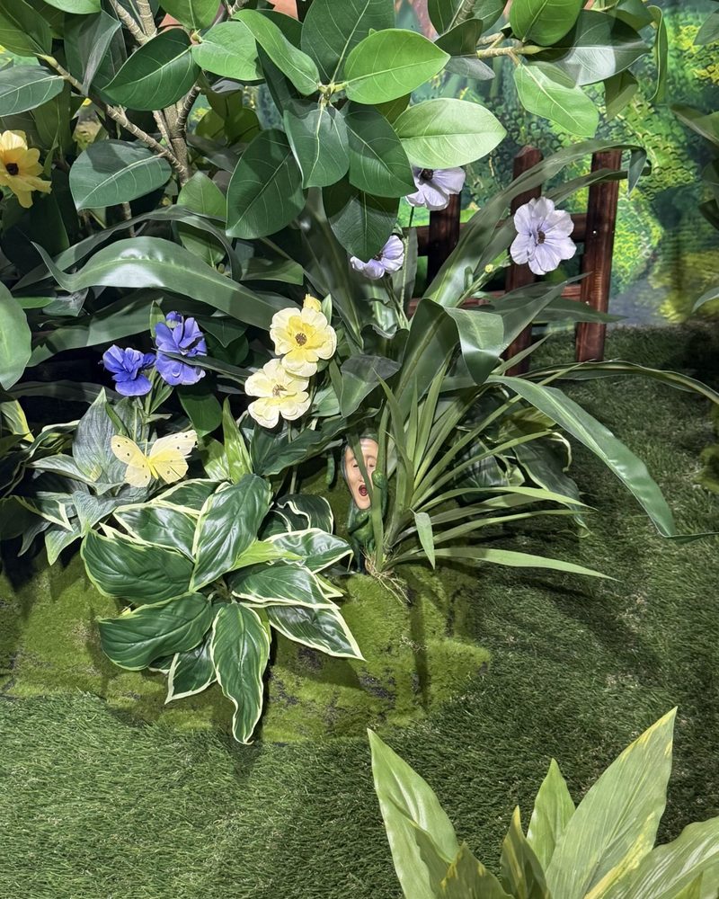 A tiny Kobito figure with a human-like face peeking out from leaves and flowers