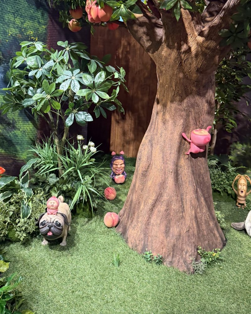 A large peach tree diorama with Kobito figures on the trunk and on the grass, and a pug statue