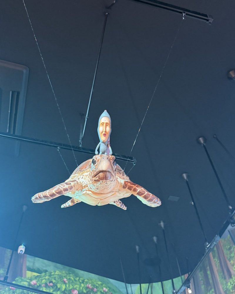 A Kobito riding on a large sea turtle model hanging from the ceiling