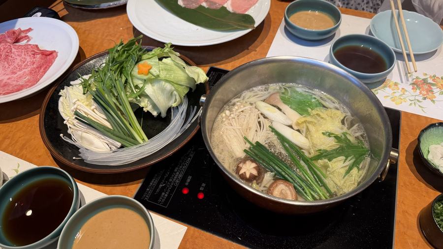 A shabu-shabu hot pot with vegetables, marbled beef, and dipping sauces